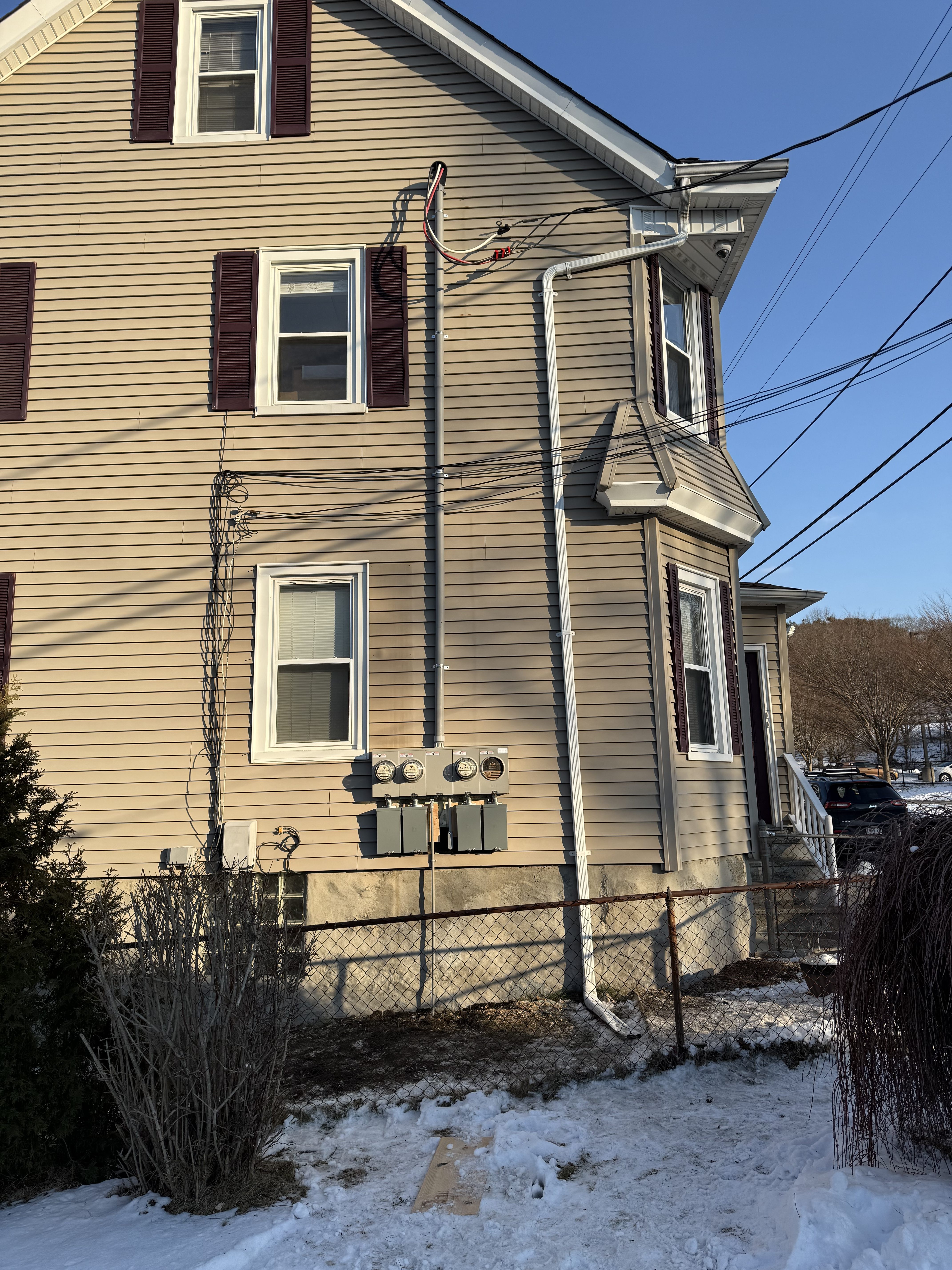 Cream two-story house with an overhead service drop and meters on the gable end, snow on the ground, North Attleborough, MA