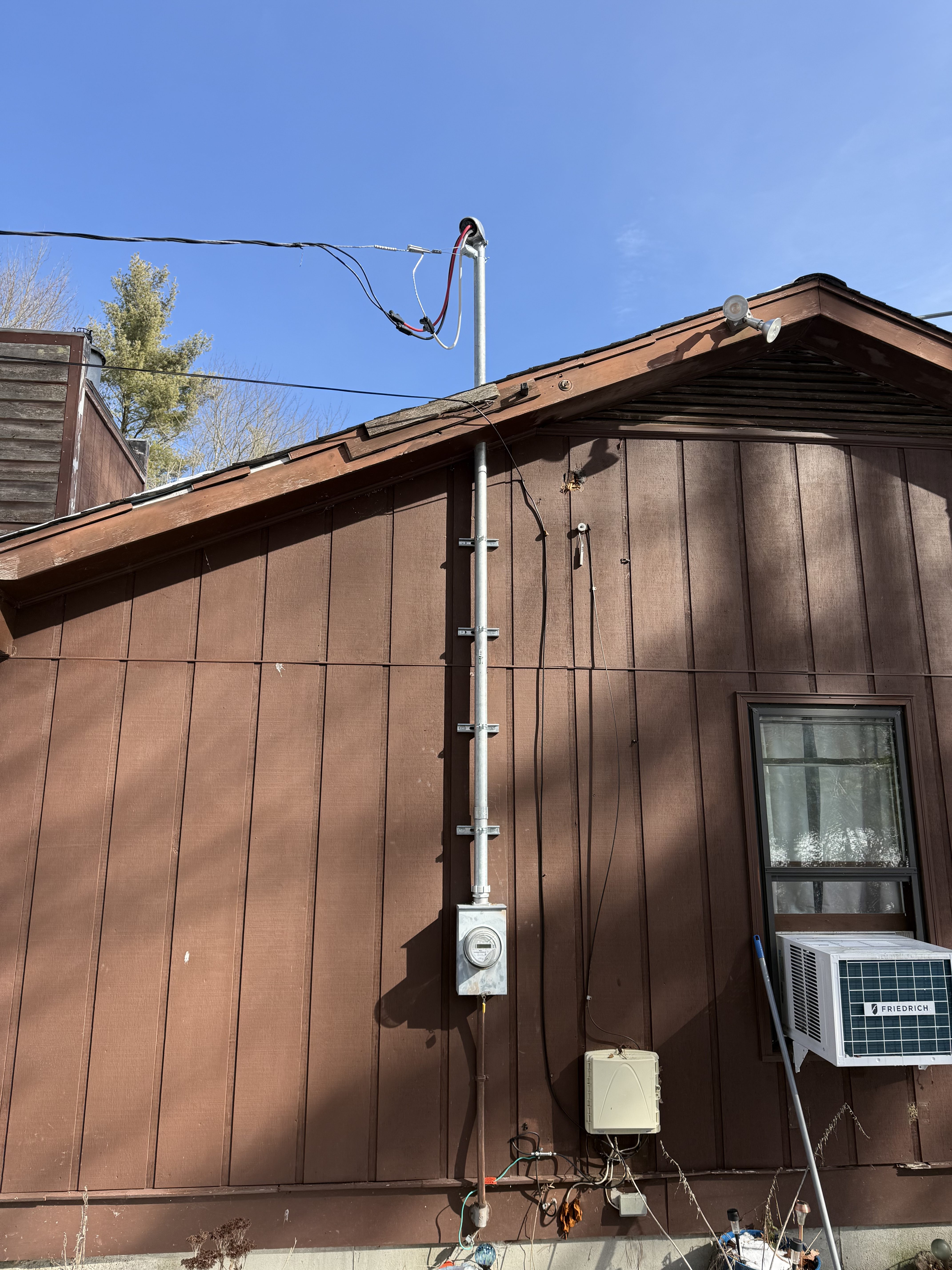 Overhead service drop, mast, conduit and meter running down the brown-sided exterior wall of a home in North Attleborough, MA