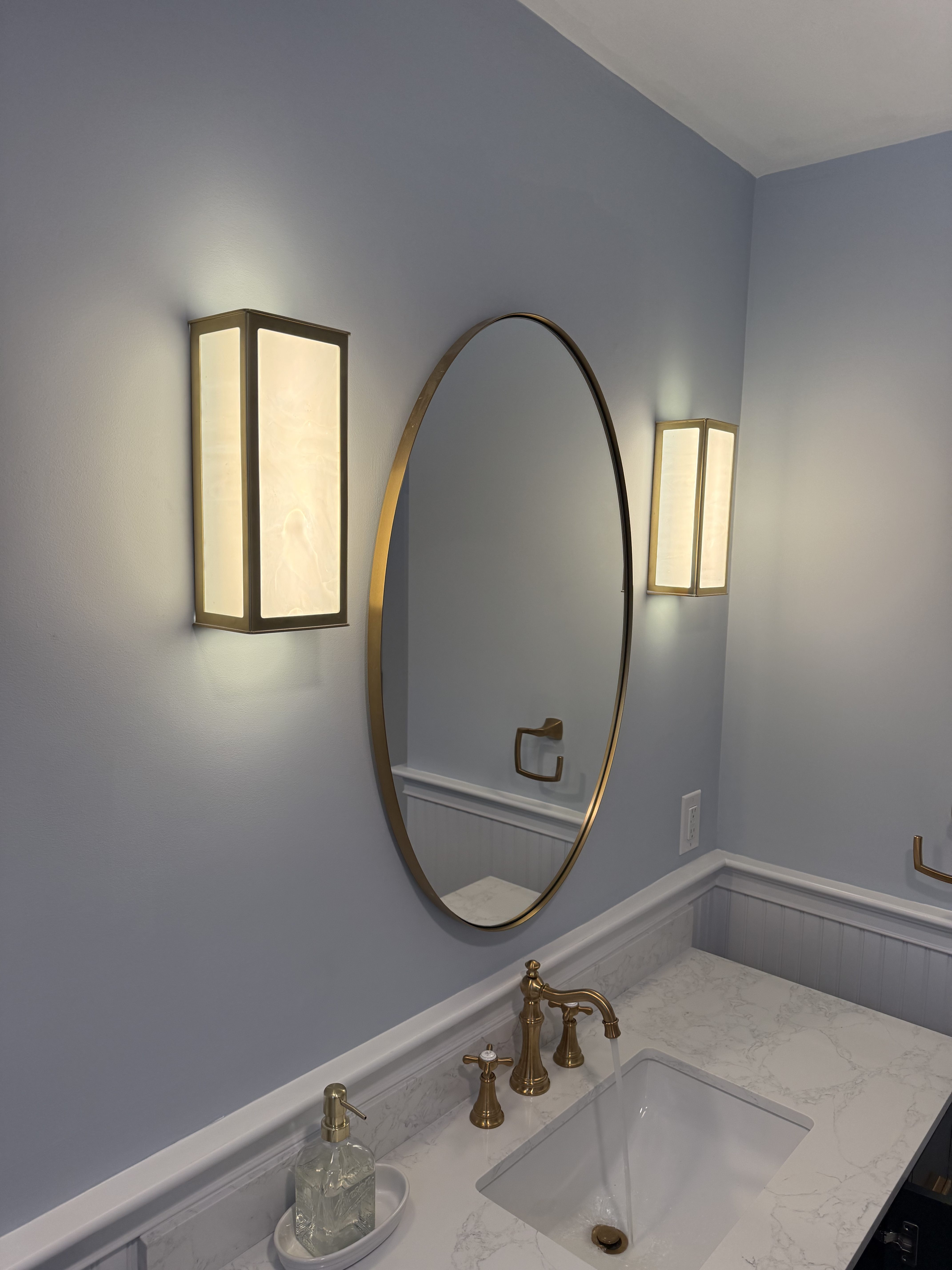 Finished powder room with a round mirror flanked by two vertical sconces above a marble vanity, North Attleborough, MA