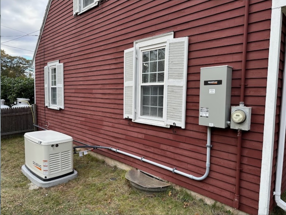 Barn-red house wall with a standby generator on a pad below a meter and disconnect, North Attleborough, MA